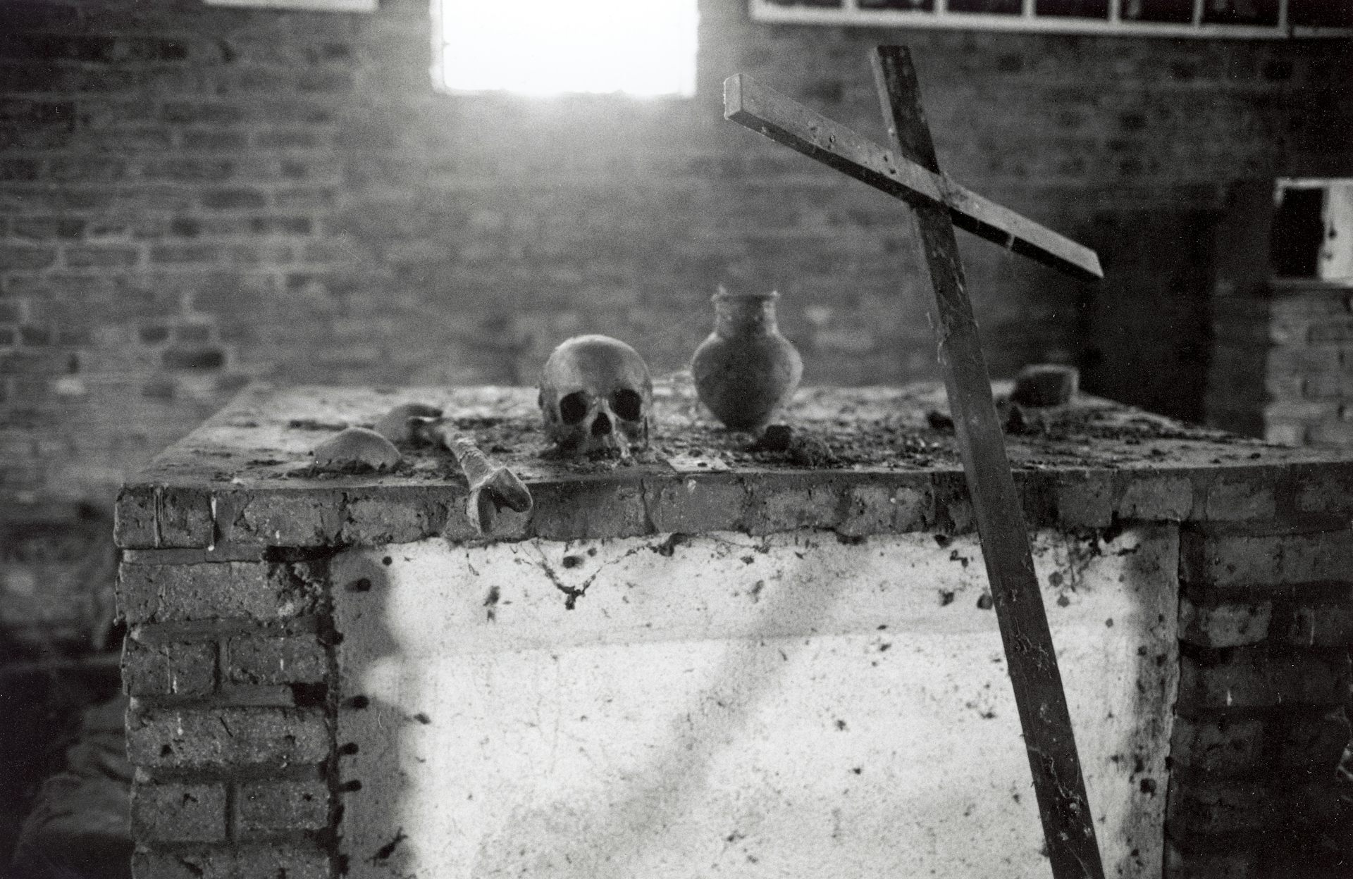 A human skull and a wooden cross lie on a brick table.
