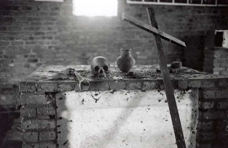 A human skull and a wooden cross lie on a brick table.