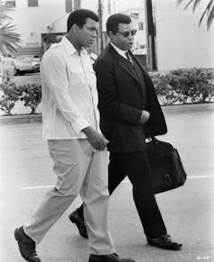 Two Black men chat while walking.