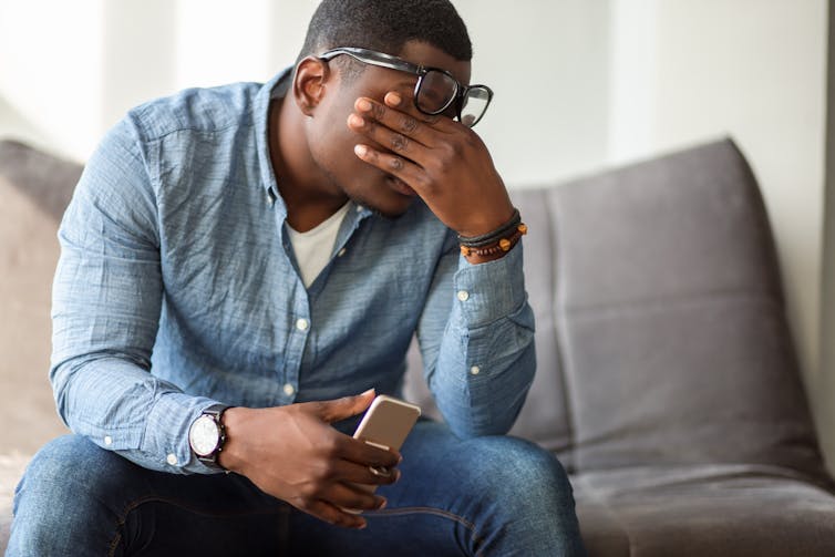 A stressed man sitting on a couch with his hand on his face.