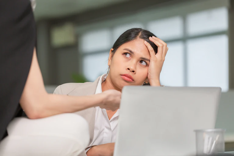 A woman has her head in her hand as she is reprimanded by a coworker.