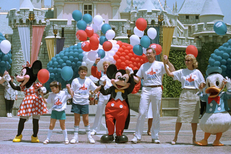 A line of people and mascots hold hands and are surrounded by red, white and blue balloons.