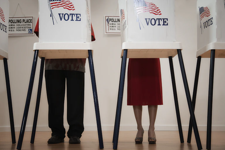 People stand at tables with barriers around them so others can't see how they're voting.