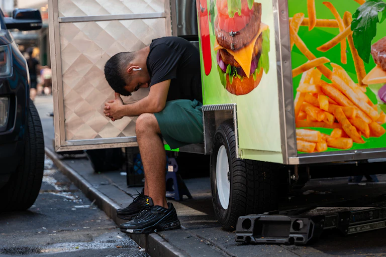 A food truck worker puts his head down while resting on the step during an NYC heat wave in June 2024.