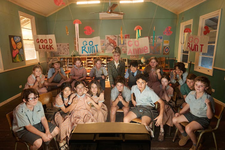School children anxiously gather around a television.