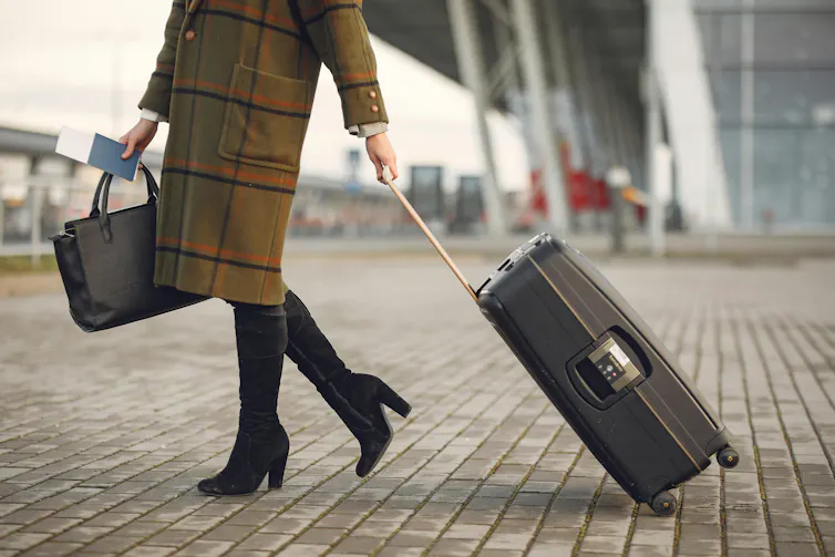 Businesswoman walking with suitcase near airport terminal