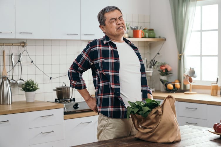 Man with back pain in kitchen, shopping on counter