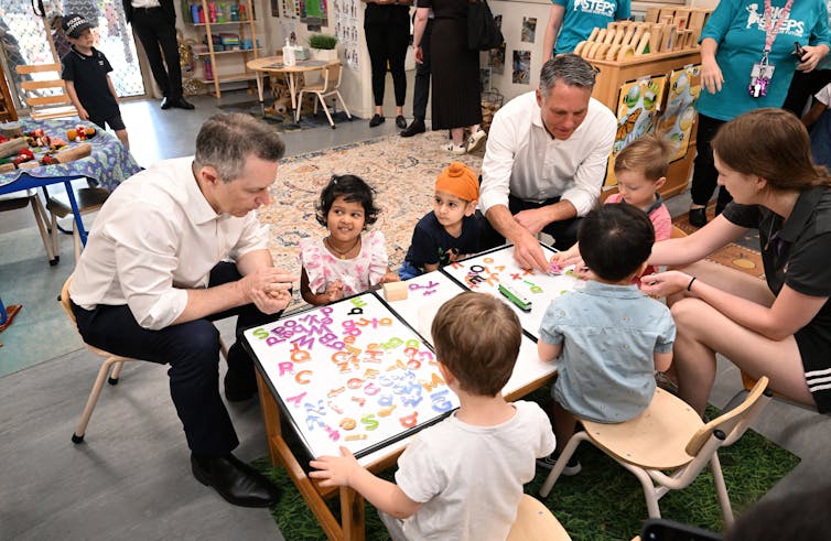Education Minister Jason Clare sits at a desk with young children at a childcare centre.