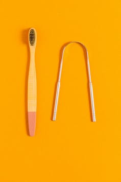 A toothbrush and a silver tongue scraper on an orange background.