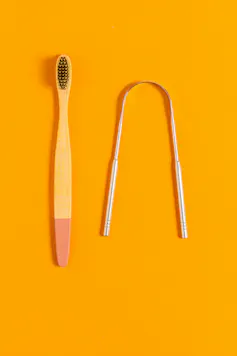 A toothbrush and a silver tongue scraper on an orange background.