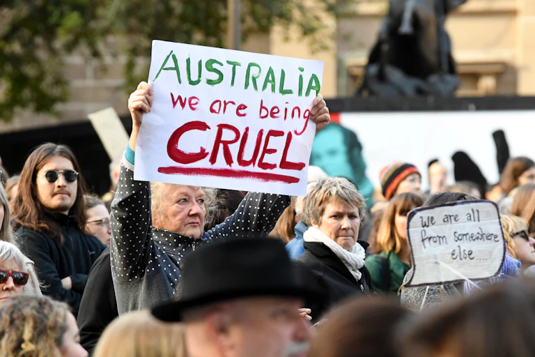 Protestors against mandatory detention, one holding banner 'Australia we are being cruel', another 'We are all from somewhere else'