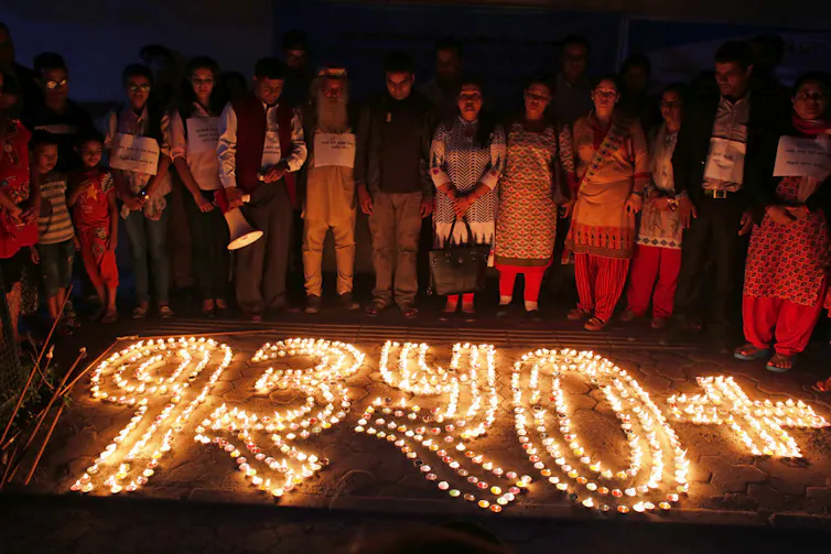 People stand in front of a candle memorial.