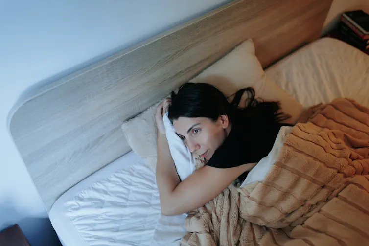 A woman lying on her side in bed looks towards a bright window.