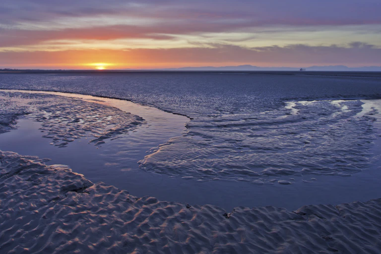 sunrise shot with orange sun and big wide grey/blue mudflats at low tide