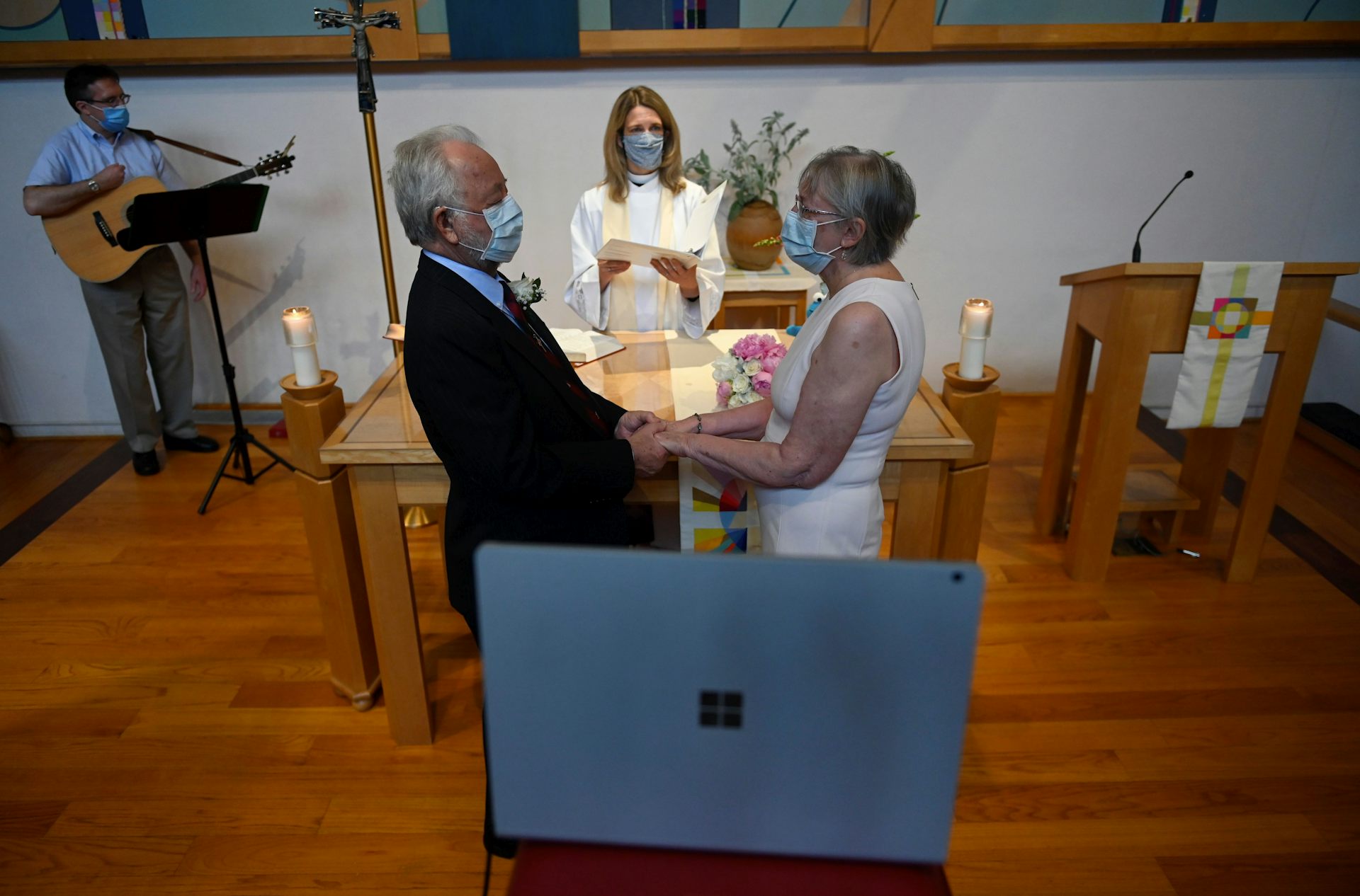 An older couple gets married over Zoom in a mostly empty church with people wearing masks.