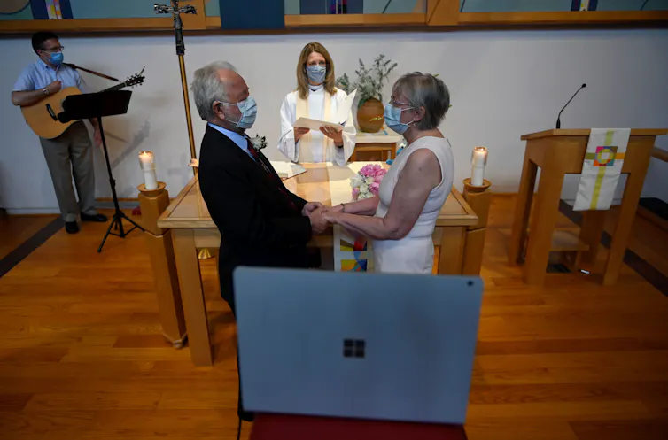 An older couple gets married over Zoom in a mostly empty church with people wearing masks.