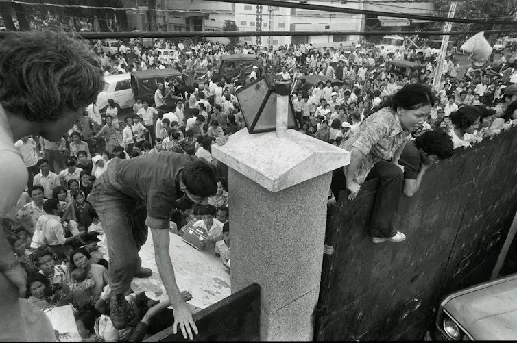 People scrambling up a wall amid a crowd.