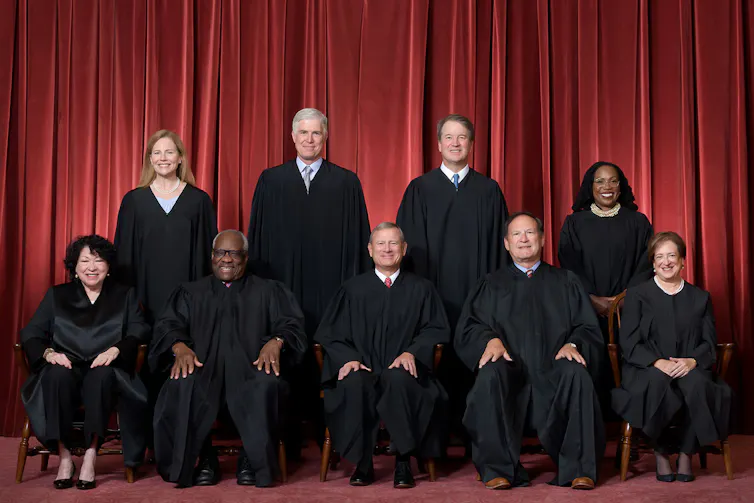 Nine people all wearing black robes, some standing and some seated.