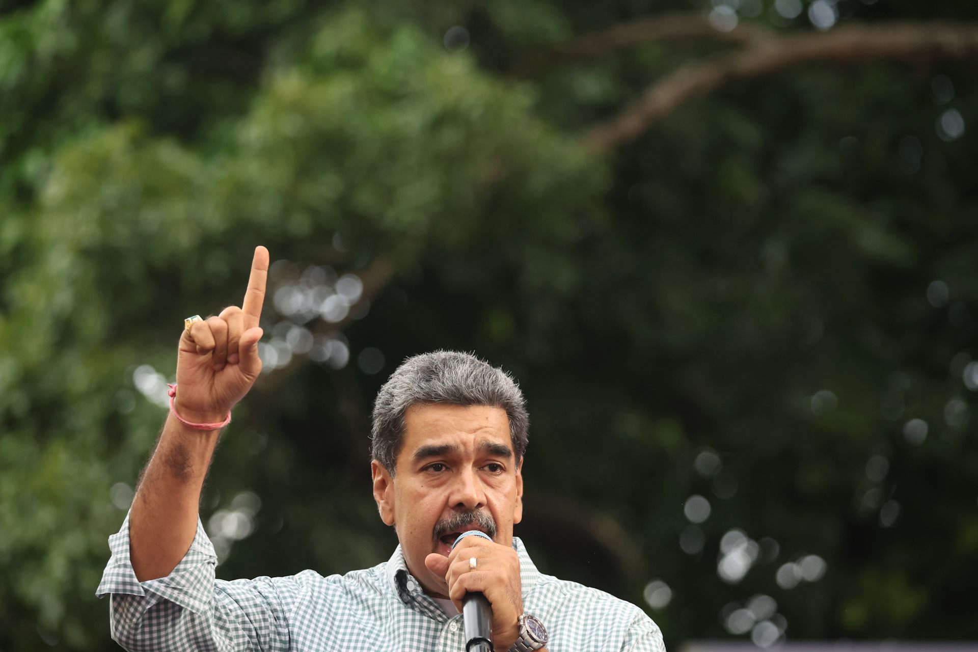 Nicolas Maduro speaking into a microphone with one finger pointing to the sky.