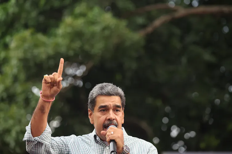 Nicolas Maduro speaking into a microphone with one finger pointing to the sky.