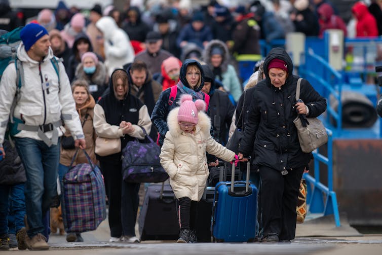 A crowd of Ukrainian refugees walking down a street with their belongings.