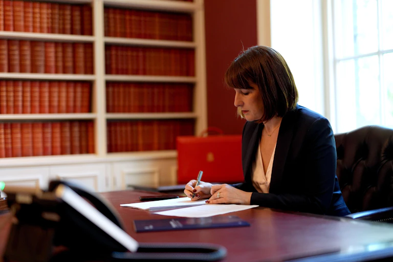 UK chancellor Rachel Reeves at her desk with red briefcase behind her