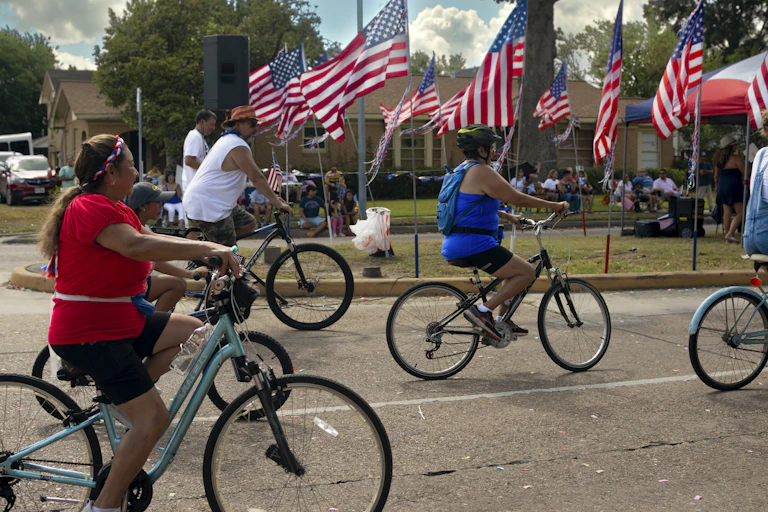 People ride bicycles past a yard filled with American flags