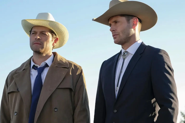 Two middle-aged men in suits and cowboy hats standing next to teach other. One is wearing a trench coat.