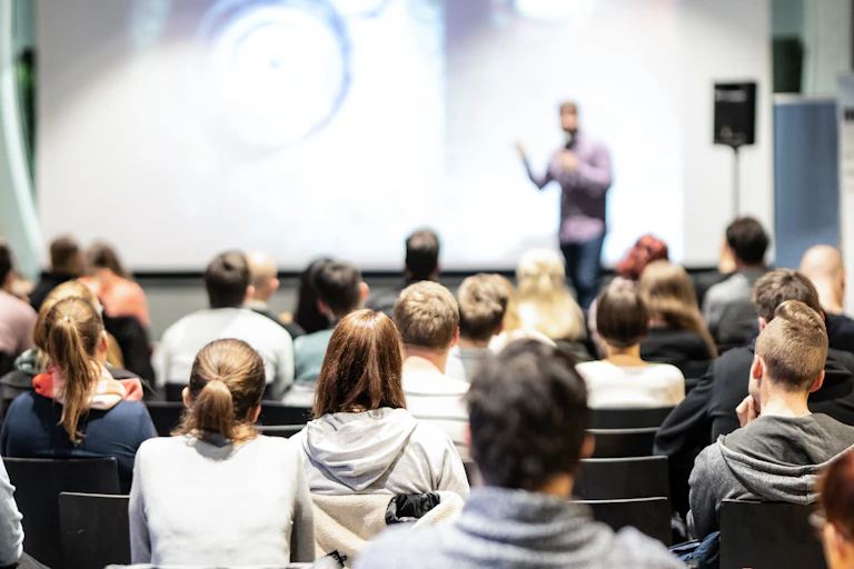 Young people sit in rows facing a person presenting.
