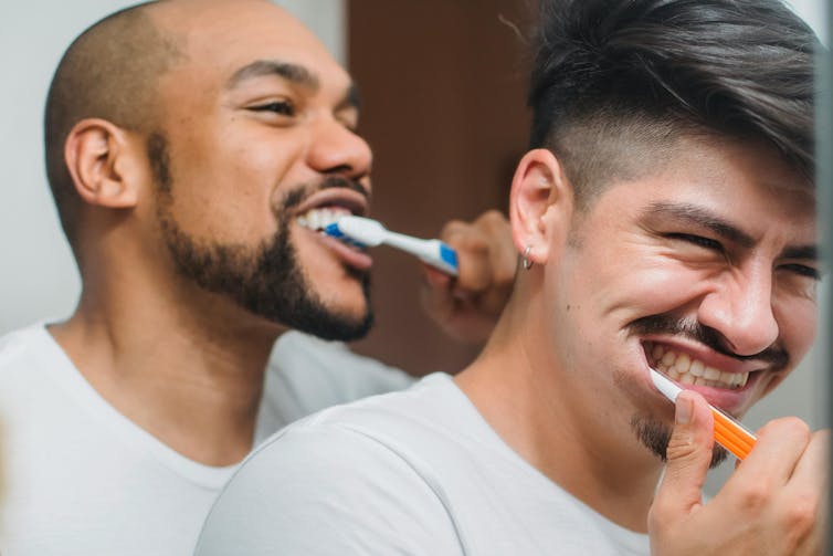 Two young men laughing while they brush their teeth.