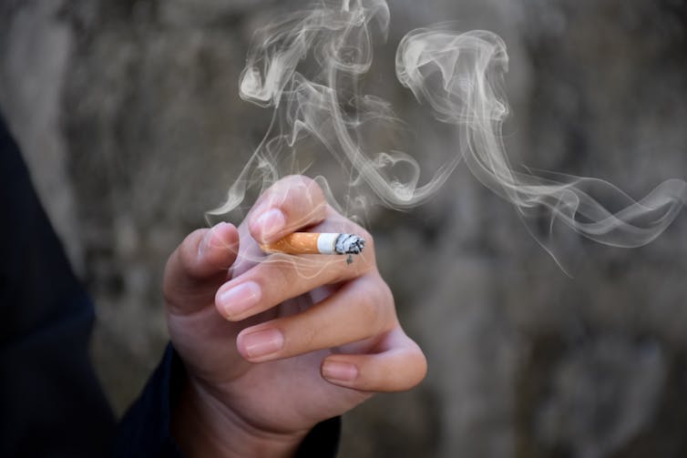 Smoke wafting from a cigarette in a woman's hand.