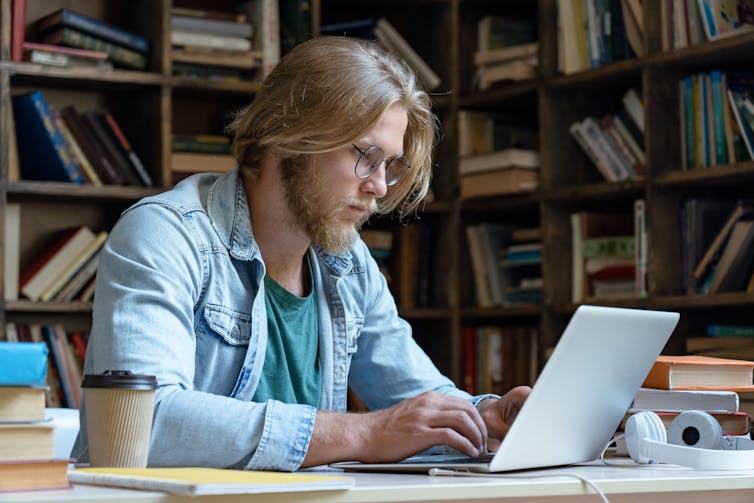 A young man working on a laptop in a library.