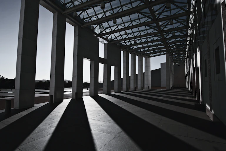 The pillars of parliament house cast a shadow on the pavement