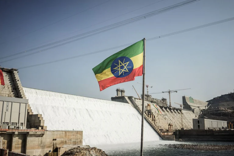 A green, yellow, red and blue flag flying in front of a massive dam wall