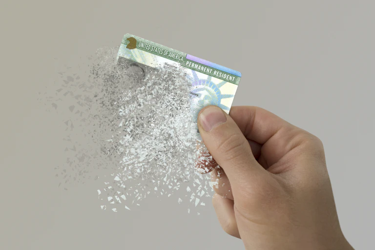 A hand holds a disintegrating green card reading 'United States of America, Permanent Resident.'