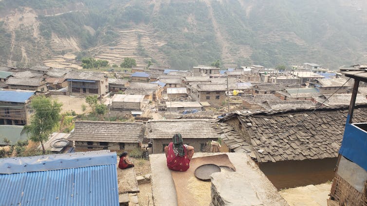A woman sits on a platform overlooking rolling hills.