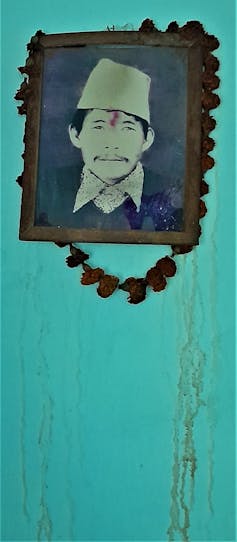 A picture of a man in a frame hangs on a green wall.