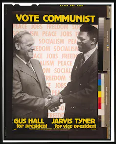 A poster shows two men shaking hands and smiling, and reads 'vote communist.'