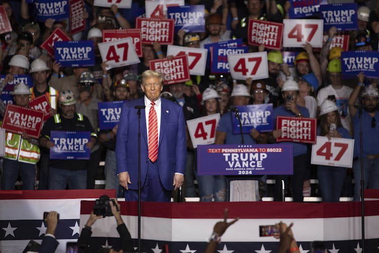 Trump stands in front of a crowd holding '47' and 'fight, fight, fight' signs