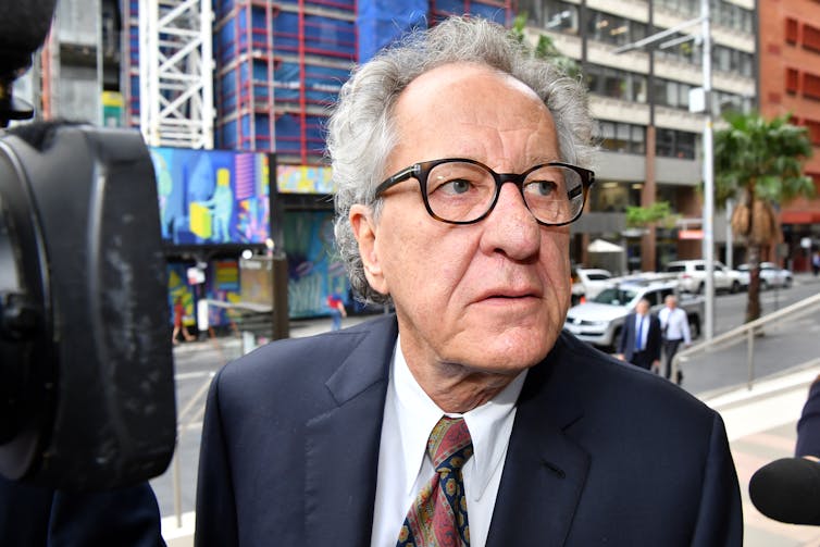 The head and shoulders of a man in glasses and a suit in a city