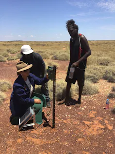 three people standing around a square device on pole
