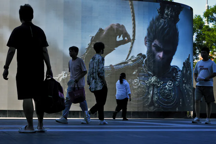 People walk past a screen promoting an advertisement of the latest blockbuster new Chinese video game 'Black Myth: Wukong'