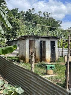A toilet block outside with mountains and trees behind.