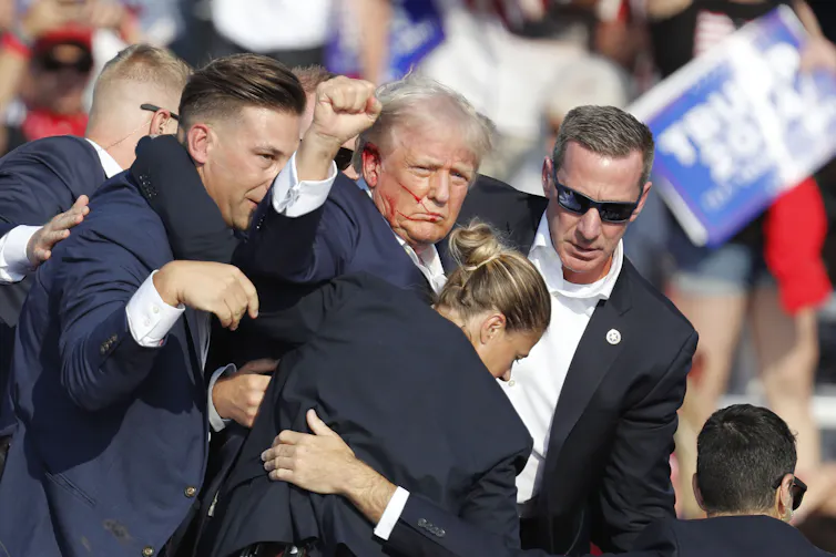 Donald Trump being rushed off stage by secret service agents with blood coming from his ear.