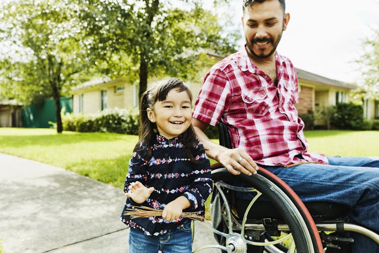 Laughing daughter out for walk through neighborhood with father in wheelchair