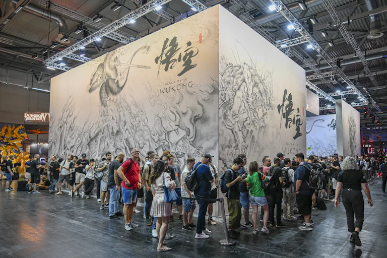 Long lines of people outside a stand, with a large drawing of a monkey and other figures and words in Chinese characters and in Enlish, which say, 'Black Myth: Wukong,'