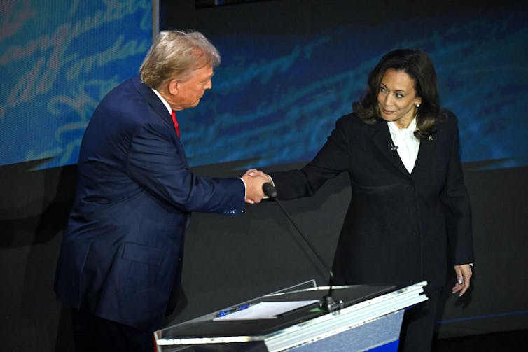 A man and a woman shake hands on a stage.