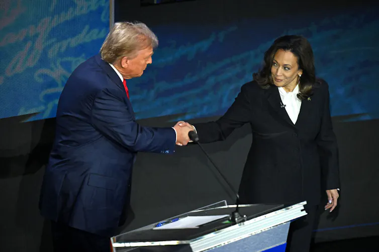 A man and a woman shake hands on a stage.