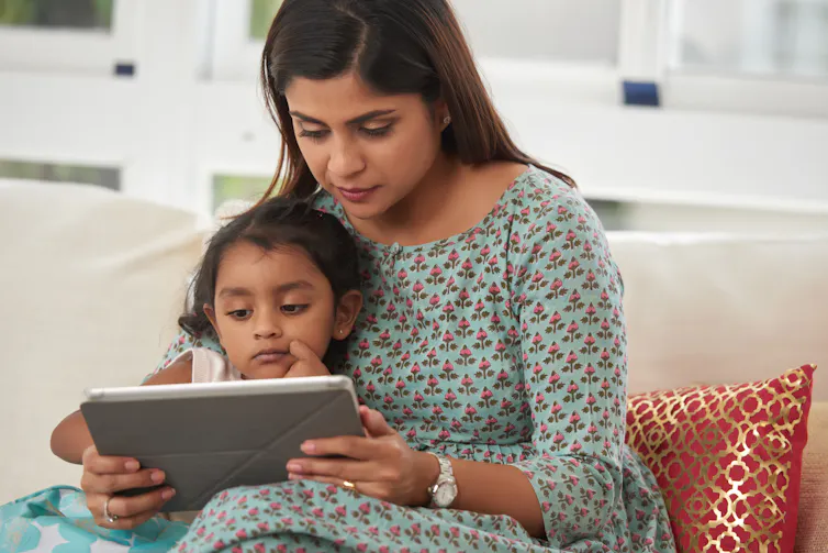 A woman and a toddler on a sofa looking at a tablet together