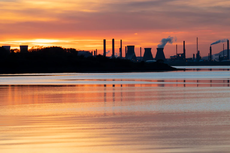 the sun sets behind the chimneys at grangemouth oil refinery